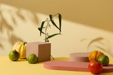 Balkabağı, domates, yeşil hurma ve sarı arka planda boş podyumlarla süslenmiş yapraklı sonbahar çiçekleri. Ön manzara, reklam fotoğrafı ve boş alan.