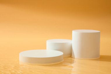 Geometrik şekilli üç beyaz podyum seti düzenlendi. Platformlar kozmetik ürün sunumu. Güzellik ürünleri için turuncu arkaplan