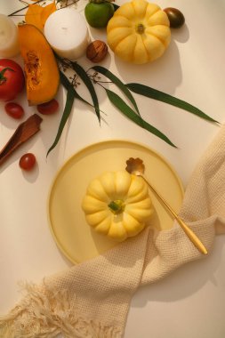 Autumn ve Şükran Günü reklam konseptiyle yaratıcı bir sahne. Beyaz bezle süslenmiş sarı seramik kabak, bej arka planda düşmüş meyve ve kurutulmuş fındık..