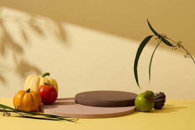 Reklam ürünleri için soyut minimal sahne. Sarı arka plandaki boş kürsülerde boş alan. Balkabakları, domates ve yeşil hurma, sonbaharın meyveleridir. Ön görünüm