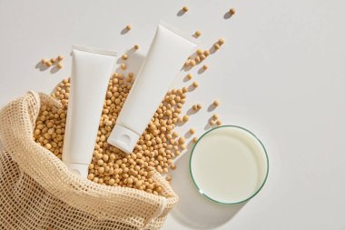 Soya çekirdekleri ve soya sütüyle dolu bir petri kabıyla sergilenen etiketsiz iki tüp. Yüz kremi, temizleyici, vücut losyonu veya şampuan için beyaz kozmetik tüp.