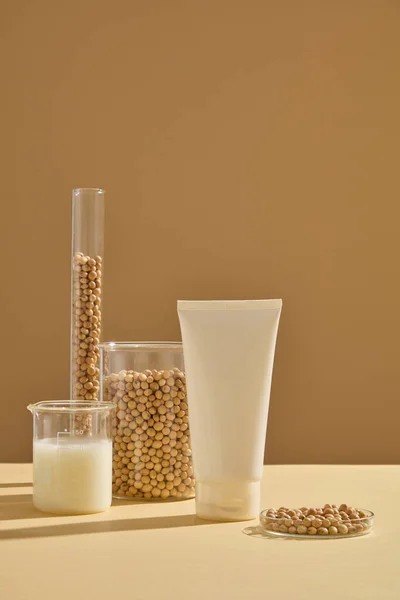 大豆と大豆ミルクの実験室ガラス製品で装飾された白い化粧品チューブ 大豆はメラニンの形成を下げる能力のために非常に普及しています — ストック写真