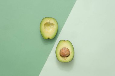 Avokado özünden kozmetik ürünlerle reklam ve markalaştırma için minimalist sanat arka planı. Avokado taze yarımlarının üst görüntüsü koyu ve açık yeşil arka planda sergilenir