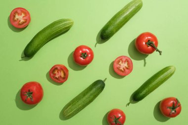 Salatalık ve domatesler yeşil arka planda sıralanır. Düz yatıyordu. Domateslerin birçok sağlık faydaları vardır çünkü antioksidan ve C vitamini içerirler.
