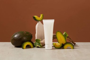 Kahverengi arka planda kozmetik tüp ve avokado dilimleri olan yaratıcı bir düzen. Tasarım ambalajı için etiketsiz bir şişe. Doğal özlü kozmetik reklamı sahnesi