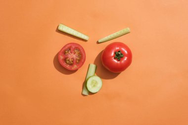 Farklı salatalık dilimleri turuncu arka planda domateslerle düzenlenir. Domates ve salatalık cilt tahrişini azaltmak için iyi bir seçimdir.