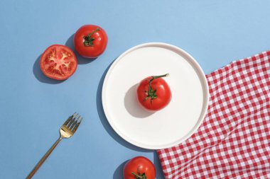 Yuvarlak şekilli, çatal, kırmızı ve beyaz kareli kumaşla süslenmiş bir domates. Domates (Solanum lycopersicum) mükemmel bir C vitamini kaynağıdır.