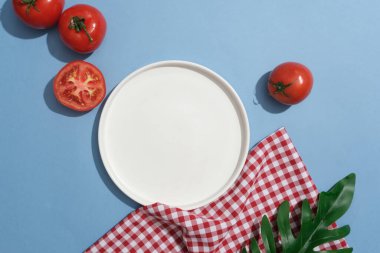 Boş tabak ve domateslerle sergilenen kırmızı ve beyaz kareli kumaş ve yeşil yaprak. Domatesin cilt için faydalarından biri hasarlı derinin onarılmasına yardımcı olmasıdır.