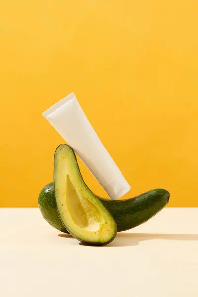 新鮮なアボカドと黄色の背景にアボカドスライスに置かれた白いプラスチックボトルのフロントビュー 健康な肌と髪のための自然なアボカドスキンケア製品 広告写真 — ストック写真