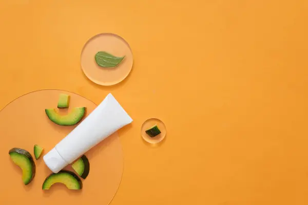 Body care beauty product packaging. Product presentation with fresh avocado slices on orange background. Top view, blank space for design or add text. Minimalist concept with avocado