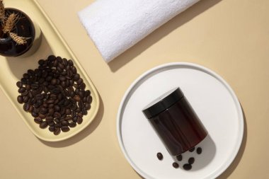 Bej arka planda, kozmetik kavanoz maketi ve malzeme kahve çekirdekleri seramik tabaklarda beyaz havluyla sergileniyor. Tasarım ambalajı, organik kozmetik reklamları için sahte şişe.