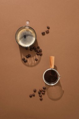 Kahverengi arka planda kahve çekirdekleri ve kahve tozu ile sergilenen bir fincan kahvenin üst görüntüsü. Gün boyunca uyanık kalabilmek için kahve reklamı yapmak için minimum bir sahne.