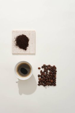 Kahve çekirdekleri ve kahve tozu tuğla podyumda, beyaz arka planda lezzetli bir fincan espresso ile süslenmiş. Reklam için minimalist konsept, ferahlatıcı bir içecek için doğal malzemeler