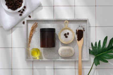 Gri mermer tepsi kabının üst görüntüsü organik malzemeli kehribar kozmetik kavanozu kahve çekirdekleri, kahve tozu, banyo tuzu ve beyaz fayansların arkasındaki buğday. Reklam için model