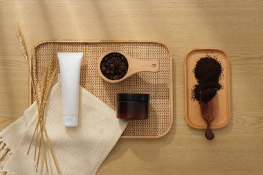 Kozmetik veya kahve içerikli ürünler sunumu için minimalist yaratıcı arka plan. Plastik tüp ve kehribar kavanozu tepside, fasulye ve ahşap zemin üzerinde kahve tozu ile sergileniyor.
