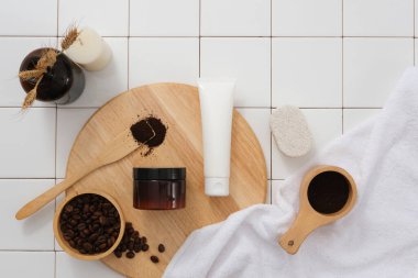 Yuvarlak ahşap kesim tahtasının üzerinde kahve çekirdekleri ve kahve tozuyla sergilenen kozmetik seti. Reklam için beyaz fayanslı banyo konsepti. Cilt bakımı güzellik ürünleri paketleme