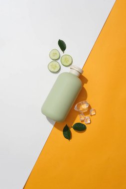 Beyaz ve turuncu arka planda salatalık, buz ve yeşil yapraklı bir kozmetik tüp vardı. Doğal kozmetik konsepti. Marka modelleme için boş etiket