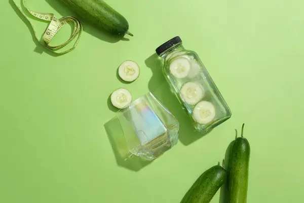 デトックスウォーターと新鮮なキュウリのボトルで配置されたホログラムガラスの平らな層 テープの測定が表示されました クッカーは栄養豊富な野菜です — ストック写真