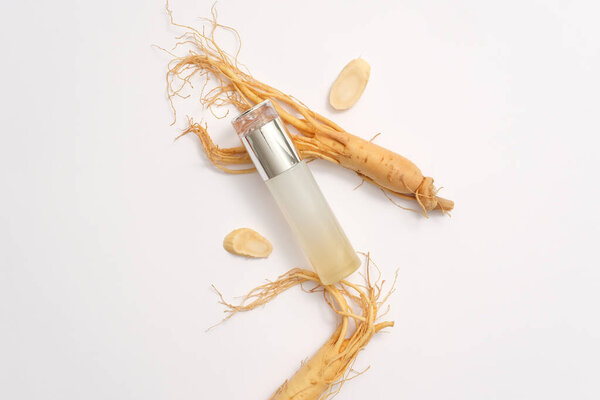 Top view of empty bottle displayed with fresh ginseng roots on white background. Ginseng is a widely used ingredient in cosmetics with many benefits for the skin. Advertising photo