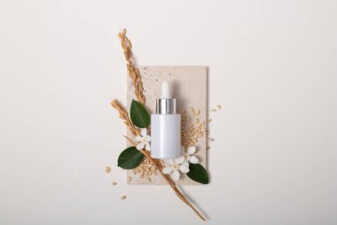 Kürsüde tam tahıllı pirinç, yeşil yapraklar ve kamelya çiçekleriyle beyaz bir serum kavanozu sergileniyor. Pirinç kepeği bileşimi, antioksidan etkisi olan phytosterol içerir..
