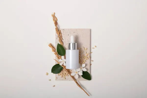 stock image A white serum jar is displayed on a podium with whole grain rice, green leaves and camellia flowers. The composition of rice bran contains phytosterols - which have antioxidant effects.