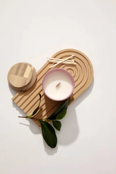 A jar of scented candles is placed on a domed wooden platform with cotton swabs and green leaves on a white background. Enjoy relaxing moments with the scent of candles.