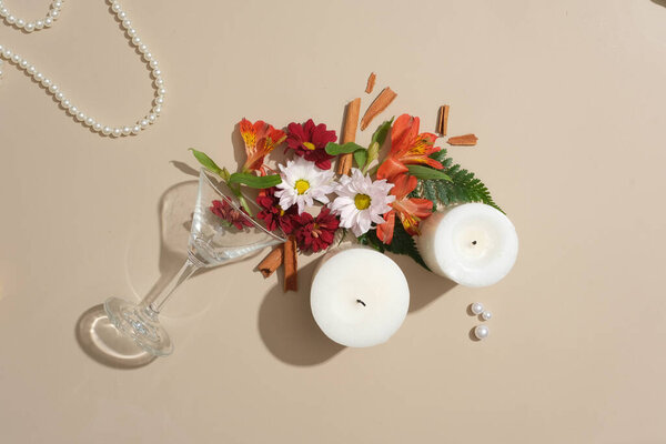 Close-up of two white candles with fresh flowers, cinnamon, a cocktail glass and a string of pearls displayed on a pastel background. Beauty theme.