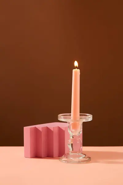 燃えているピンクのろうそくのフロントビューは 茶色の背景を持つピンクのテーブルの上にガラスのろうそくとピンクの表彰台に置かれています プロダクト表示のためのスペース — ストック写真
