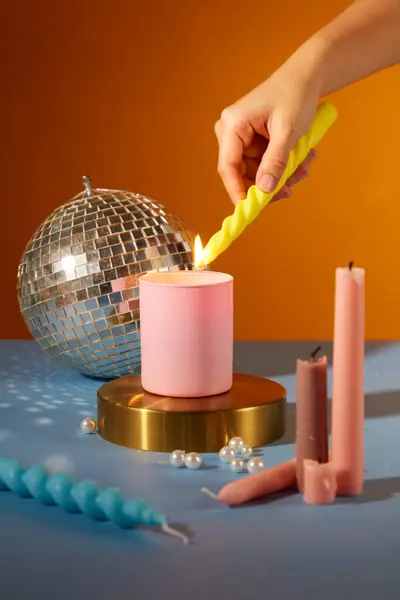 Close up of woman hand lighting candles on colorful background. Candles, pearls and a disco ball decorated on the table. Party atmosphere. Creative space for ads.