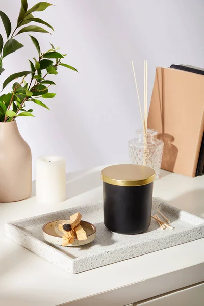 盘子里有一罐有香味的蜡烛和燃烧的木棍 陶瓷花瓶 绿色的叶子和白色背景的道具 精美的广告空间 — 图库照片