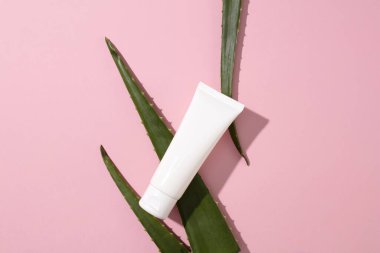 Etiketlenmemiş bir losyon tüpünün yukarıdan görüntüsü pembe arka plandaki aloe vera yapraklarına yerleştirilir. Doğal kozmetik reklamları için bir model. Doğal güzellik..