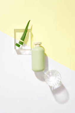 Etiketsiz bir kozmetik şişe, bir bardak su ve taze aloe vera pastel arka planda cam bir podyumda sergilenir. Reklamcılık için yaratıcı alan.