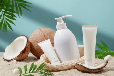 Etiketsiz beyaz kozmetik seti. Yeşil yapraklar ve hindistan cevizi ile beyaz kum zemininde sergilenen taze hindistan cevizinin ana malzemesi. Doğal kozmetik ürünleriyle cilt bakımı.