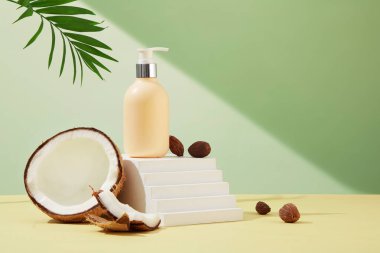 Yeşil yapraklar ve hindistan cevizi ile dekore edilmiş merdiven şeklindeki bir platforma püskürtülmüş açık sarı duş jeli şişesi yerleştirilir. Ürün reklamcılığı için minimalist sahne.