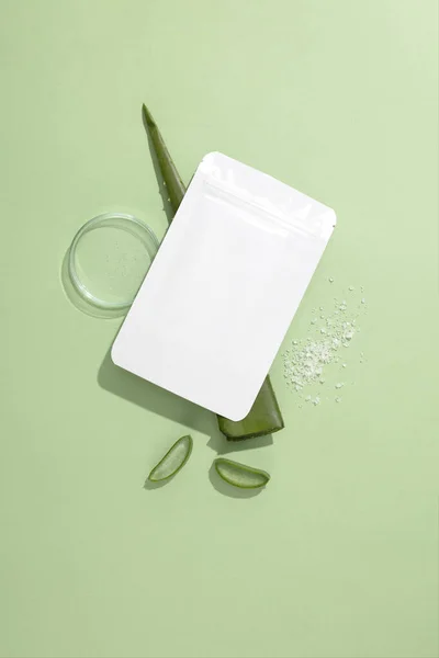 Close-up of an unbranded mask sheet placed on a fresh aloe vera leaf, next to a transparent petri dish on a pastel background. Mockup for cosmetic brand advertising.