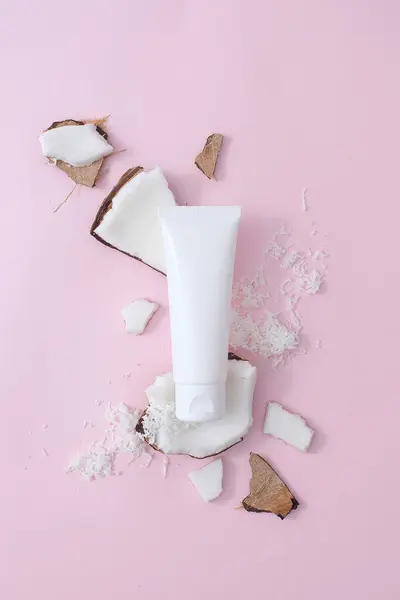白いプラスチックの化粧品の管はピンクの背景に新鮮なココナッツの部分に置きました 新鮮なココナッツエキスの化粧品コンセプト 広告のためのシーン — ストック写真