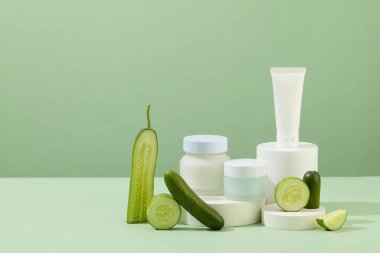 Marka etiketi olmayan kozmetik şişeleri beyaz bir podyuma yerleştiriliyor. Taze salatalıklar kenara konur. Salatalık özünden alınan ürünlerle cilt bakımı.