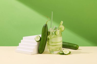 Merdiven şeklinde beyaz podyum, salatalık ve minimalist arka planda bir bardak detoks suyu. Sahne donanımı ve taze meyvelerle reklam alanı oluşturun. Serinlik ve tazelik.