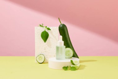 Taze salatalık ve perilla yaprakları pembe-sarı arka planda bir şişe cilt bakım serumunun yanında sergilenir. İyi besin değeri yüksek ve cilt için güvenli iki bileşenin karışımı..