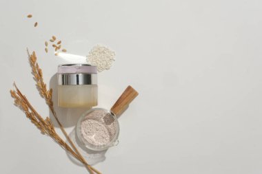 Zarif bir şekilde tasarlanmış kozmetik kavanoz pirinç tozu ve pirinçle beyaz bir zemin üzerinde sergileniyor. Boş etiketler yaratıcı markalaşma ve reklam için yer sağlar.