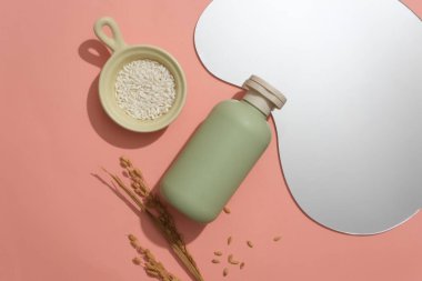 Pastel yeşili kozmetik şişesi, fasulye şekilli ayna ve pembe zemin üzerinde seramik tabakla birlikte pirinç. Reklamcılık ve güzelliğin temel unsurları için mükemmel bir yer..