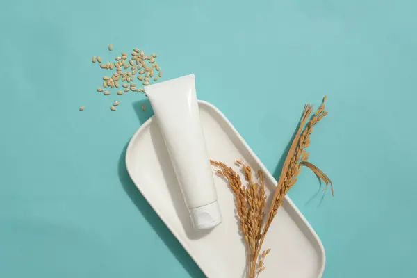 皿に小麦耳で飾られたラベルのない化粧チューブ ほんの一握りの小麦の種子が紹介されました 自然な美容製品の広告のための空のラベルチューブ — ストック写真