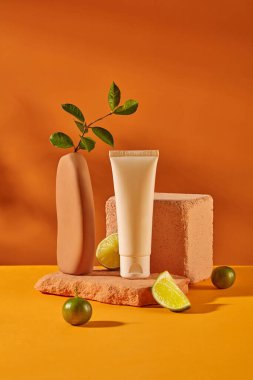 Etiketsiz bir kozmetik tüpü, limon ve kumkatlarla çevrili taş bir platforma yerleştirilir. Parlak arka plan, sarı ve turuncu renkler. Kozmetik Model.