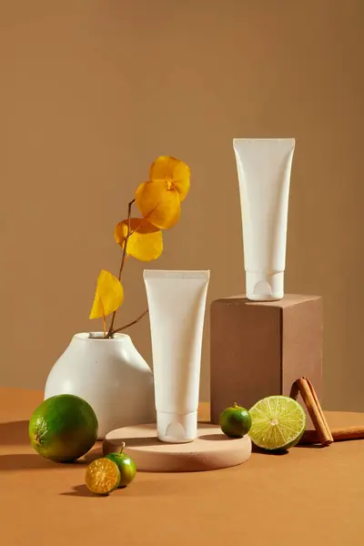Front view of two cosmetic tubes placed on a wooden platform, fresh lemon, cinnamon and autumn leaves on a brown background. Ideal scene for cosmetics advertising.