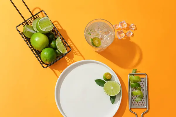 柠檬和Kumquat放在一个铁筐里 一杯加冰的水 一个加Kumquat皮的研磨机和一个橙色背景的白色陶瓷盘 广告的复制空间 — 图库照片