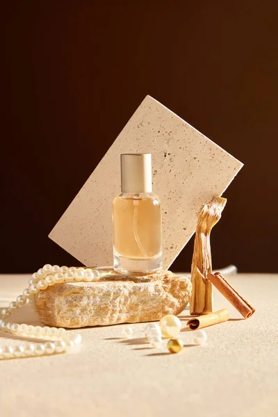 为香水产品做广告的场景和设计的模型 一个玻璃瓶在一块石头装饰珍珠项链 肉桂棒和白色砖片的褐色背景 — 图库照片
