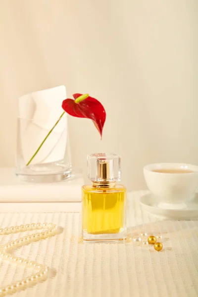一个黄色香水瓶的前视图展示在米黄色的背景与红花花瓶 一杯咖啡和珍珠项链 设计造型的精油产品广告场景 — 图库照片