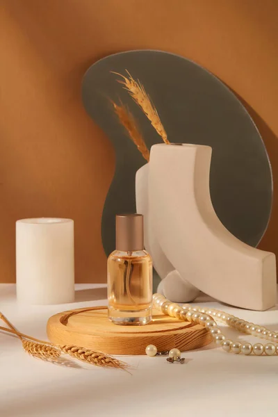 Background for branding and packaging presentation perfume product. A glass bottle without label on wooden podium displayed with pearl necklace, candle and wheat on brown background. Front view