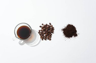 Beyaz arka planda bir fincan sade kahve, kahve çekirdeği ve kahve tozu. Kahve içmek bazı hastalıkların önlenmesinde ve azaltılmasında etkilidir..