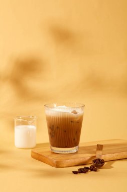 Sütlü kahve fincanının ön görüntüsü ahşap bir platforma yerleştiriliyor, hemen yanında bez bir arka planda süt ve kahve çekirdekleri yer alıyor. Yiyecek ve içecek reklamı sahnesi.